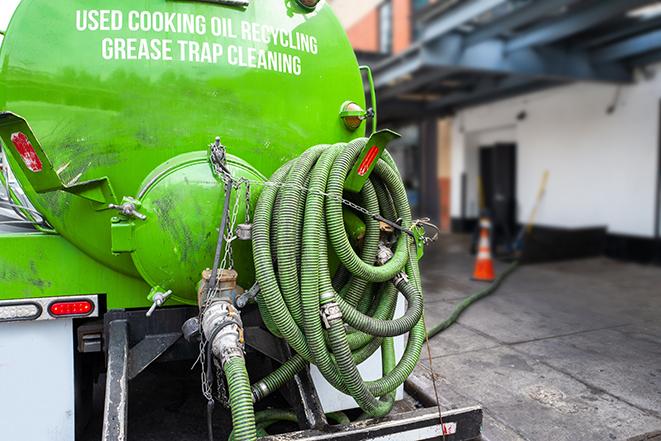 a professional plumber using a pump to empty a grease trap in East Los Angeles, CA